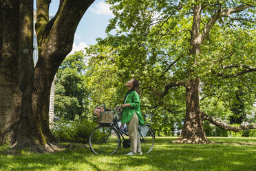 Frau mit Fahrrad, die am Wochenende im Park an einem Baum steht - NDEF01217