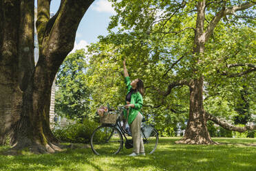 Frau mit Fahrrad an einem Baum im Park stehend - NDEF01218
