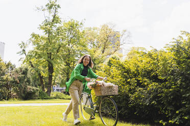 Frau mit Fahrrad bei Pflanze im Park am Wochenende - NDEF01221