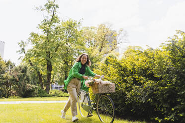 Woman with bicycle by plant in park on weekend - NDEF01221