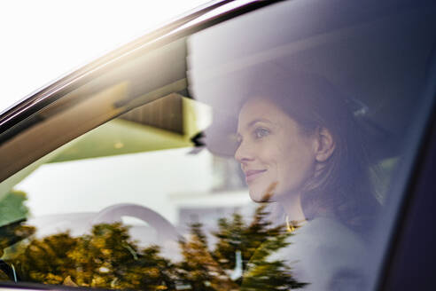 Lächelnde Frau, die ein Elektroauto fährt, gesehen durch ein Fenster - DIGF20880