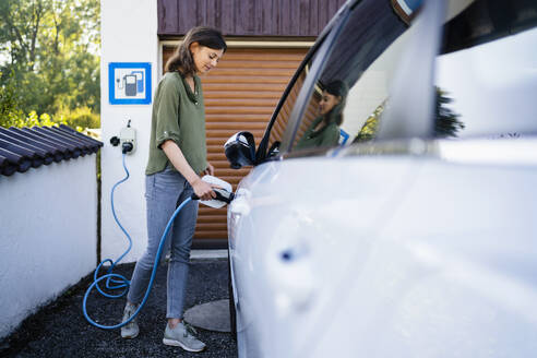 Ältere Frau lädt Elektroauto mit Stecker an einer Station auf - DIGF20883