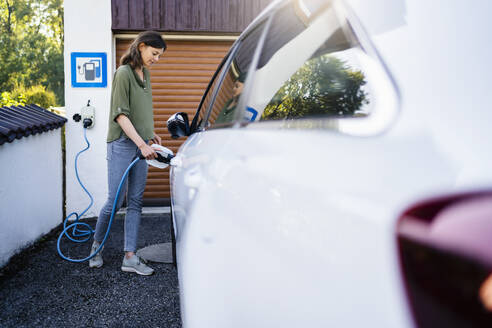 Frau lädt Elektroauto an der Tankstelle auf - DIGF20884