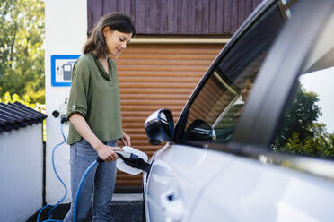 Ältere Frau lädt Elektroauto mit Stecker auf - DIGF20885