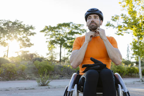Sportler, der seinen Helm im Rollstuhl sitzend befestigt - JCCMF10855