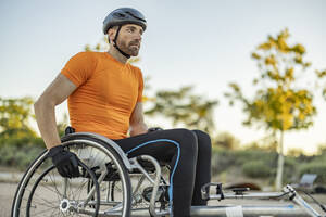 Contemplative athlete sitting on wheelchair at sunset - JCCMF10868