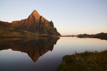 Scenic view of calm lake surrounded by Anayet mountain range against cloudless blue sky during sunset in Pyrenees - ADSF48180