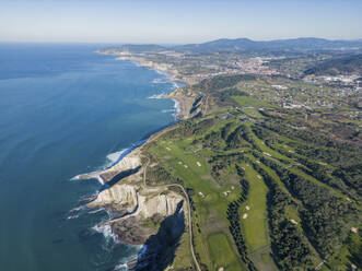 Breathtaking drone of verdant Basque coast with rocky cliff against green waving sea with foam in sunshine - ADSF48216