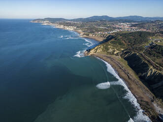 Aerial view of tranquil sea with verdant water near green Basque shore on sunny day - ADSF48218