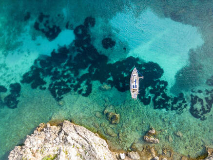 Aerial top view of transparent turquoise water of sea on Menorca island with floating sailboat on surface - ADSF48220