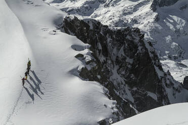 Top view of anonymous people in warm clothes and skis walking on fresh white snow on winter day - ADSF48254