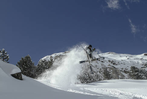 Side view of anonymous man jumping with skis on snowy mountain on winter day - ADSF48258