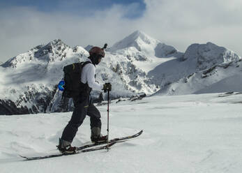 Side view of black skier in warm ski suit and with backpack strolling along snowy mountain ridge against cloudless blue sky on Ushuaia Argentina - ADSF48289