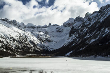 Unrecognizable skier in warm ski suit and with backpack strolling along snowy mountain ridge against cloudless blue sky on Ushuaia Argentina - ADSF48298