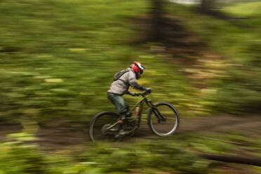 Active fearless athletic sportsman in bright protective clothes driving bike on steep road in forest - ADSF48311