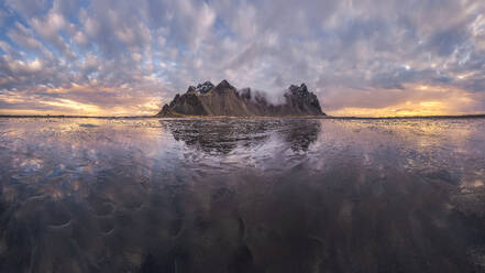 Scenic view of frozen beach against snowy mountains in winter evening sunset in Stokksnes in Iceland - ADSF48314