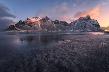 Scenic view of frozen beach against snowy mountains in winter evening sunset in Stokksnes in Iceland - ADSF48315