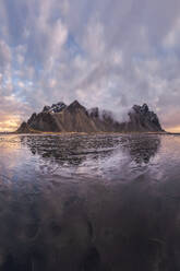 Scenic view of frozen beach against snowy mountains in winter evening sunset in Stokksnes in Iceland - ADSF48323