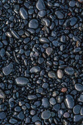 Top view of wet stones located near smooth sedimentary rock on coast in Reynisfjara Beach - ADSF48352