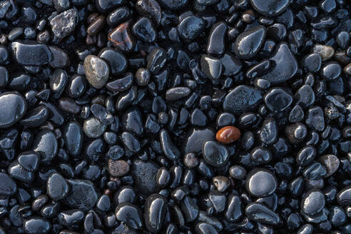 Top view of wet stones located near smooth sedimentary rock on coast in Reynisfjara Beach - ADSF48353