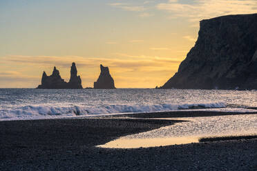 Picturesque view of dark foamy waves of ocean water against cloudy sundown sky in evening in Reynisfjara Beach, Iceland - ADSF48355