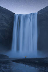 Breathtaking view of magnificent waterfall and rough cliff under beautiful sky with many sparkling stars in Skogafoss Iceland - ADSF48362