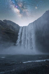 Breathtaking view of magnificent waterfall and rough cliff under beautiful cloudy sky with many sparkling stars in Skogafoss Iceland - ADSF48366