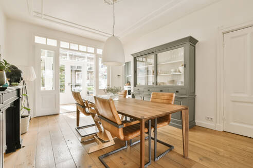 Interior of dining room with wooden table and chairs arranged while pendant light hanging from ceiling at contemporary home - ADSF48409