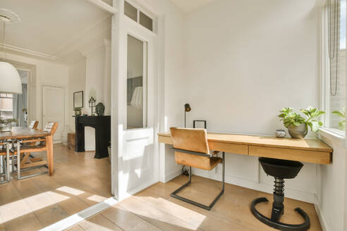 Interior of modern home office with wooden desk and empty chair in front of white wall - ADSF48411