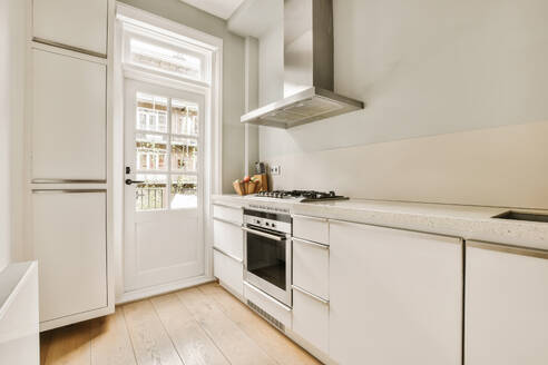 Interior of modern kitchen with chrome hood over stainless steel stove at counter and white cabinets in spacious light apartment - ADSF48413