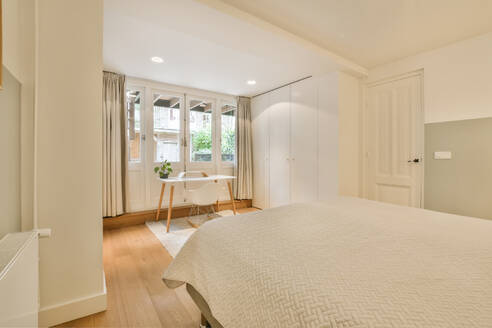 Interior of white bedroom with bed and desk in front of closed doors in contemporary apartment - ADSF48419