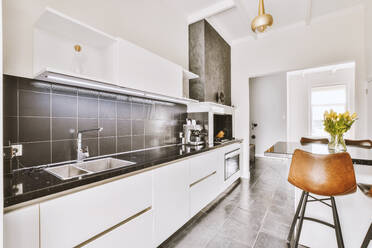 Interior of contemporary kitchen with empty chairs at table near countertop with sink and cabinet at home - ADSF48425