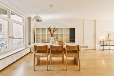 Interior of spacious modern home with dining table and wooden chairs arranged by window in dining room - ADSF48432