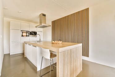 Interior of spacious kitchen with large wooden island and sink in modern apartment with white walls and cabinets - ADSF48442