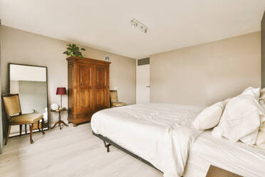 Interior of bedroom with white bed in front of wooden wardrobe and mirror at modern home - ADSF48449