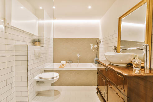 Interior of illuminated modern bathroom with toilet bowl and bathtub with tiled walls at home - ADSF48451