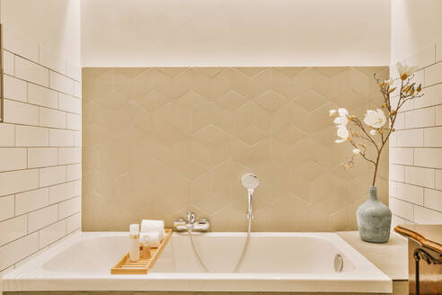 Interior of modern bathroom with bathtub and flower vase in front of patterned wall at home - ADSF48452