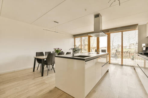 Interior of open plan kitchen with large island and dining table at contemporary home with white walls and large window - ADSF48455