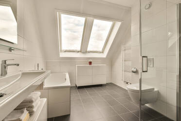 Interior of large modern bathroom with sink and bathtub by toilet seat in front window at home - ADSF48459