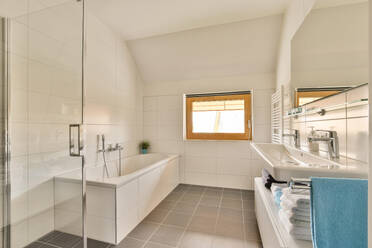 Interior of white bathroom with bathtub and sink below mirror by window at home - ADSF48460