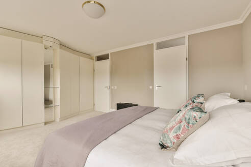 Interior of bedroom with comfortable bed in front of large white closet in modern apartment - ADSF48471