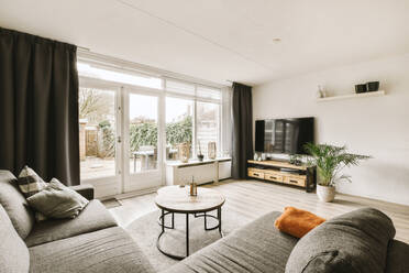 Comfortable sofa and coffee table placed in front of television by large window in modern living room - ADSF48479