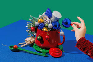 Crop anonymous female with red nails placing christmas ball in pot with different ornaments near spoon against blue and green background - ADSF48485