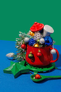 High angle of Christmas table setting with different colorful ornaments placed in red pot against blue and green background - ADSF48489