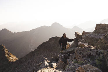 Älterer Mann beim Wandern auf einem felsigen Berg bei Sonnenaufgang - PCLF00862