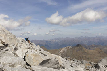 Mann sitzt auf einem Felsen unter bewölktem Himmel - PCLF00870