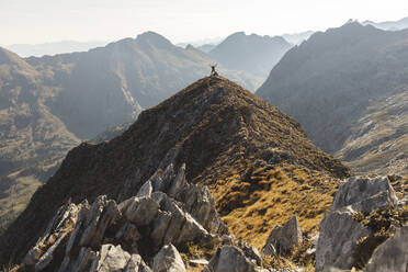 Mann steht mit erhobenen Armen auf einem Berggipfel - PCLF00874