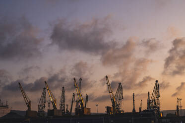 Bulgaria, Varna, Clouds over harbor cranes at dusk - ALKF00657