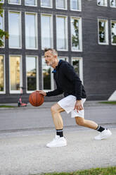 Älterer Sportler dribbelt Basketball auf dem Sportplatz - DIGF20895