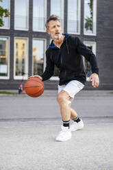 Sportsman dribbling basketball and playing on sports court - DIGF20896